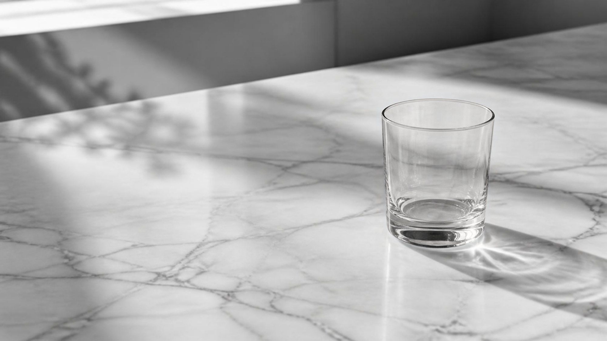 Black and white photo of a polished white marble countertop with a glass (illustrative image)