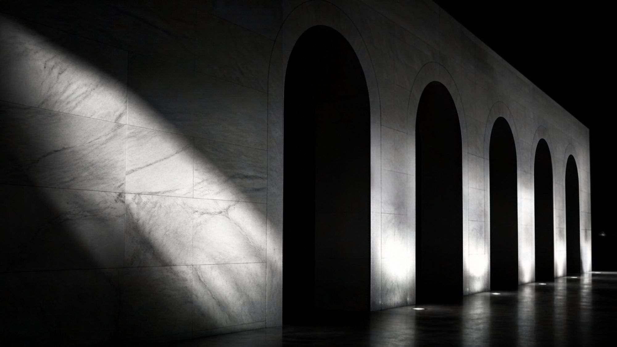Black and white image of light grazing a white marble wall with arches at night (illustrative image)