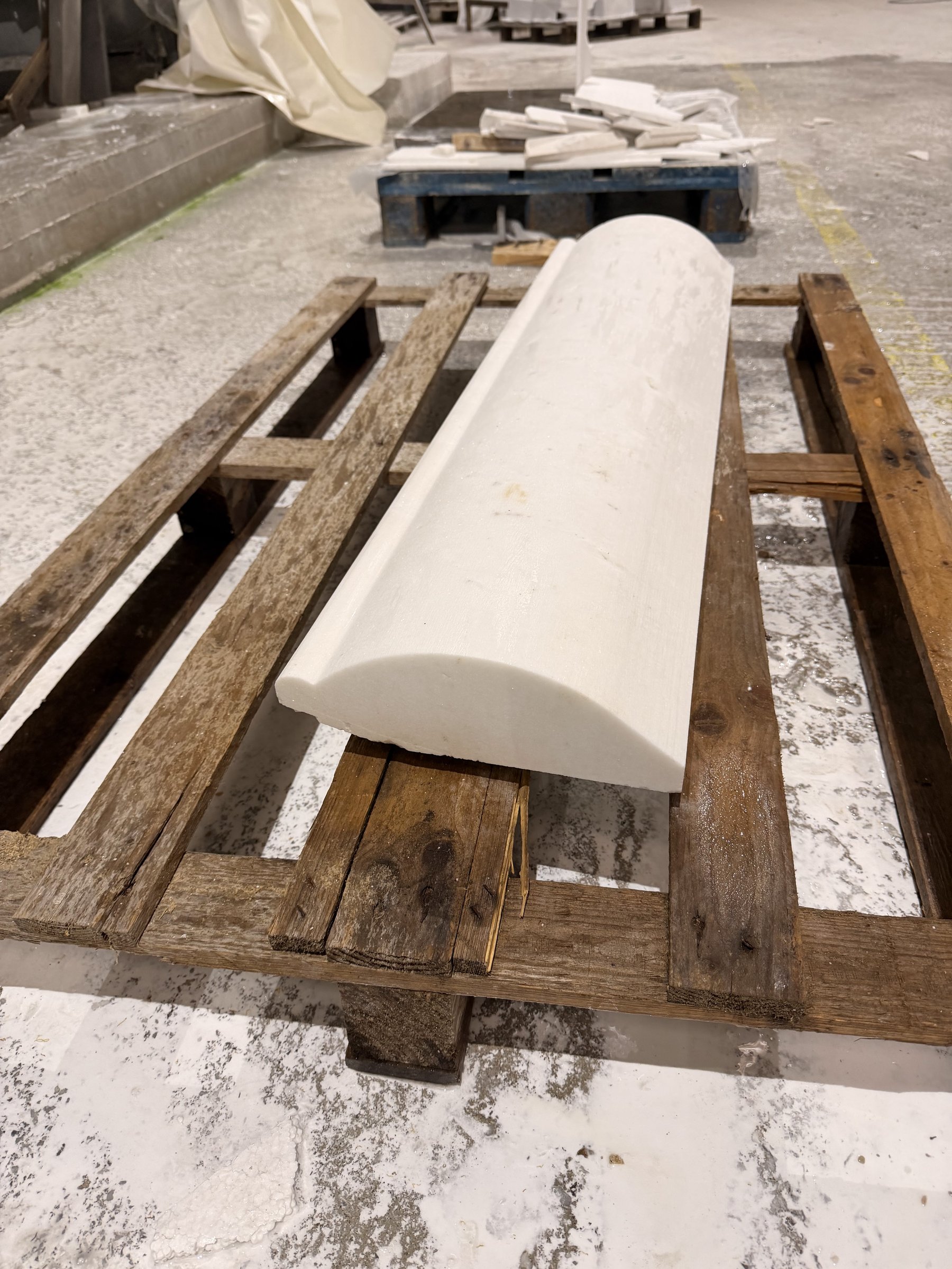 Carved white marble moulding resting on a wooden pallet in the stone workshop