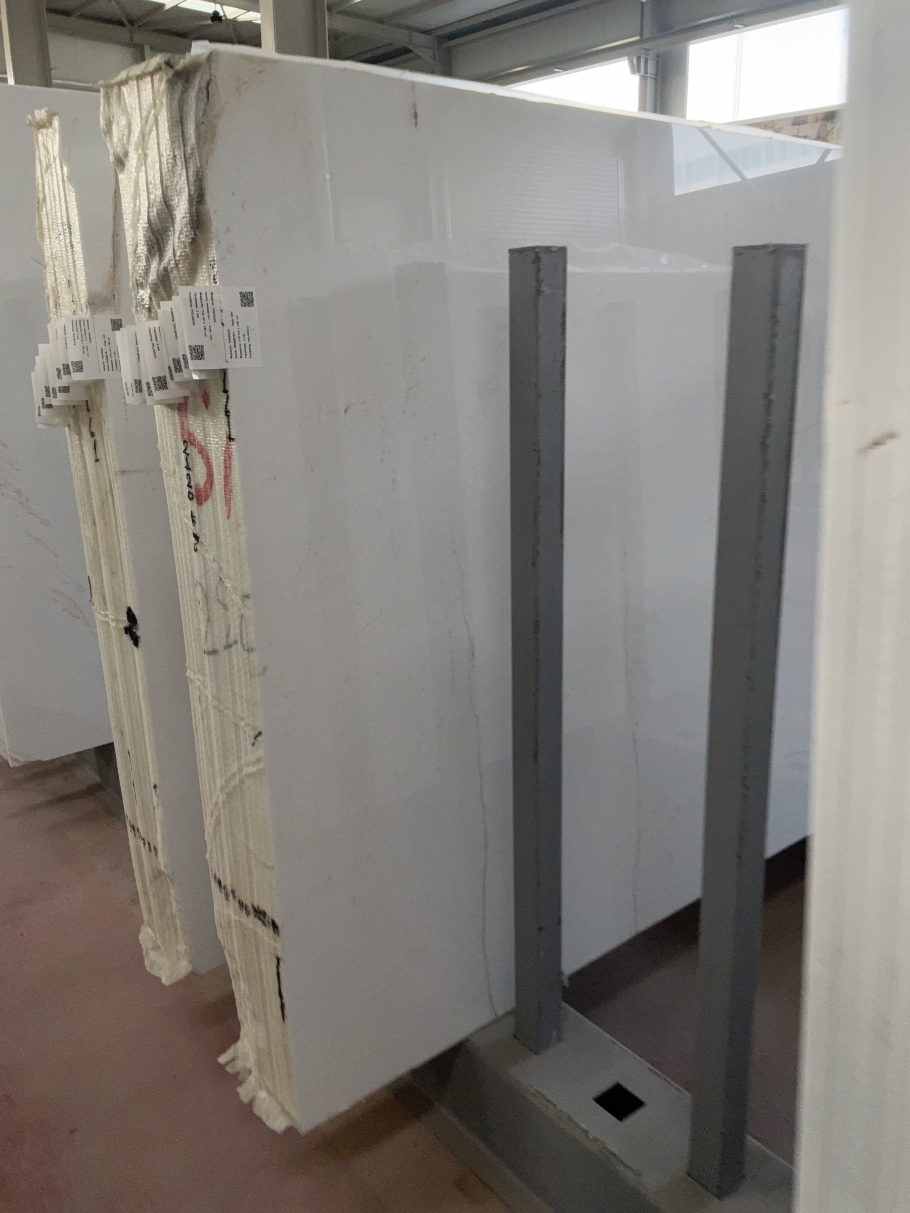 Row of bright white marble slabs with very faint veining standing in a warehouse